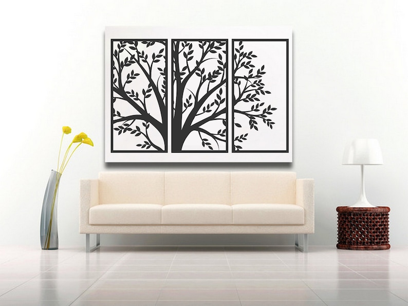 May include: A triptych wall art piece featuring a black tree silhouette with leaves against a white background. The artwork is displayed above a cream-colored sofa. A tall, slender vase with yellow flowers and a side table with a lamp are also in the room.