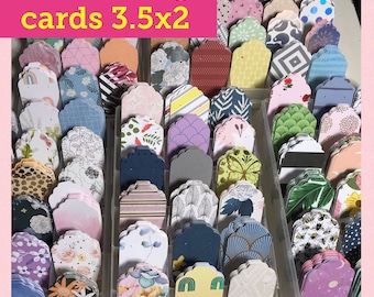 May include: 100 earring cards 3.5x2. A collection of colorful and patterned earring cards, each with a scalloped edge. The cards are arranged in rows and columns, showcasing a variety of designs.