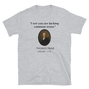May include: A light gray t-shirt featuring the quote "I see you are lacking common sense." above a portrait of Thomas Paine. Below the portrait, the text reads "- THOMAS PAINE JANUARY, 1776."