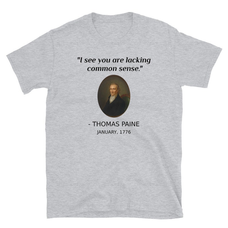 May include: A light gray t-shirt featuring the quote "I see you are lacking common sense." above a portrait of Thomas Paine. Below the portrait, the text reads "- THOMAS PAINE JANUARY, 1776."
