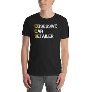 May include: A black t-shirt with white text that reads "OBSESSIVE CAR DETAILER". The "C" in "CAR" is highlighted in yellow.