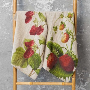 Puede incluir: Dos toallas de té de lino con estampado de fresas. Las toallas son beige con hojas verdes y fresas rojas.