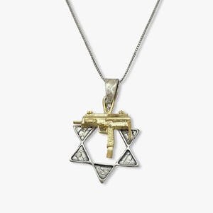 Może przedstawiać: Srebrny łańcuszek z zawieszką przedstawiającą złoty pistolet nałożony na srebrną Gwiazdę Dawida.
