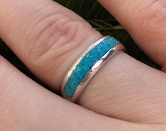 May include: A silver ring with a turquoise inlay. The ring is worn on a finger.