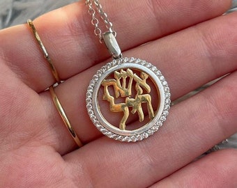 May include: A silver and gold pendant necklace with a round charm. The charm features a gold design within a silver frame, surrounded by small, clear stones. The necklace is on a silver chain.