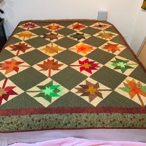May include: A handmade quilt featuring a repeating pattern of colorful leaf shapes in shades of red, orange, yellow, and green. The leaves are set against a green background with a diamond grid pattern. The quilt has a decorative border.