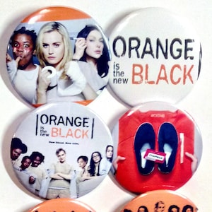 May include: Six orange and white round buttons with different designs related to the TV show "Orange is the New Black". The buttons feature the show's logo, characters, and a prison-themed design.