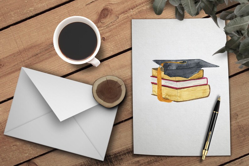 May include: A white envelope, a cup of coffee, a wooden coaster, and a white card with a watercolor illustration of a graduation cap on top of a stack of books.