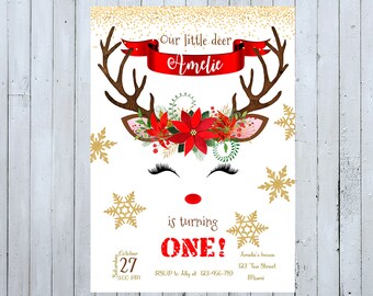 May include: A festive Christmas-themed invitation with a reindeer illustration. The reindeer has a red and green floral crown, a red nose, and eyelashes. The text reads "Our little deer Amelie is turning ONE!" with details for the party, including the date, time, RSVP information, and address.