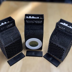 K&ouml;nnte beinhalten: Drei schwarze 3D-gedruckte Boxen mit einem wei&szlig;en Gittermuster und einem digitalen Timer auf der Vorderseite. Die Boxen haben ein wei&szlig;es Etikett mit dem Text "AirPlus Booster" auf der Vorderseite. Jede Box hat eine kleine schwarze rechteckige Basis.