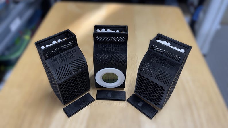 K&ouml;nnte beinhalten: Drei schwarze 3D-gedruckte Boxen mit einem wei&szlig;en Gittermuster und einem digitalen Timer auf der Vorderseite. Die Boxen haben ein wei&szlig;es Etikett mit dem Text "AirPlus Booster" auf der Vorderseite. Jede Box hat eine kleine schwarze rechteckige Basis.