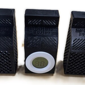 K&ouml;nnte beinhalten: Drei schwarze Kunststoff-Feuchtigkeitsabsorber mit dem Aufdruck "Moisture Buster". Der mittlere Absorber hat ein wei&szlig;es digitales Hygrometer mit einer Anzeige von 88%.