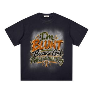 Puede incluir: Una camiseta negra de manga corta con un estampado gráfico que incluye el texto "I'm BLUNT Because God Rolled Me That Way" en letras naranjas, verdes y blancas, centrado sobre un símbolo ankh, sobre un fondo blanco suave y difuso.