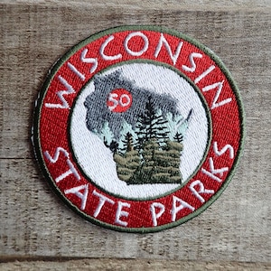 May include: Circular embroidered patch featuring the words "WISCONSIN STATE PARKS" in white on a red background. The patch includes a gray outline of Wisconsin with a "50" in a red circle, and a forest scene.