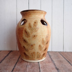 May include: A ceramic vase with a brown and yellow glaze and a leaf pattern. The vase has several holes around the middle.