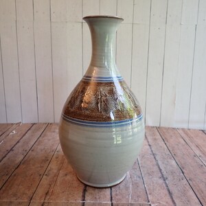 May include: A white ceramic vase with a brown and blue design. The vase has a narrow neck and a round body.