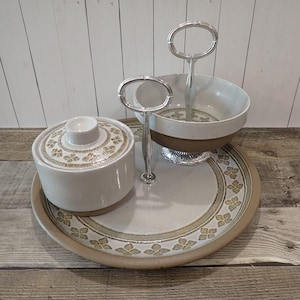 May include: A vintage ceramic serving set with a round tray, a covered sugar bowl, and a two-tiered serving dish. The set features a speckled cream and brown color scheme with floral accents and silver handles. The tray measures approximately 12 inches in diameter.