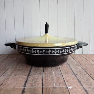 May include: A black and cream serving dish with a lid and a black knob. The dish has a decorative white pattern around the rim.