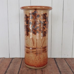 May include: A brown ceramic vase with a floral design. The vase has a light brown base and a darker brown floral pattern.