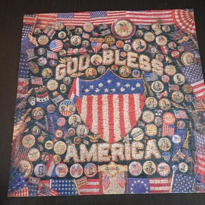Może przedstawiać: Ukończone puzzle o tematyce patriotycznej. Puzzle przedstawiają słowa "GOD BLESS AMERICA" w ozdobnej czcionce, otoczone obrazami amerykańskich flag, pieczęci patriotycznych i portret&oacute;w postaci historycznych. Schemat kolor&oacute;w to czerwony, biały i niebieski.