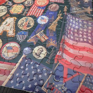 Może przedstawiać: Ukończone puzzle o tematyce patriotycznej. Przedstawiają amerykańską flagę, postacie historyczne i patriotyczne wstążki. Elementy są ze sobą połączone, tworząc kompletny obraz na ciemnym tle. Idealne na prezent.