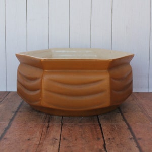 May include: A brown ceramic planter with a hexagonal shape and a fluted design. The planter has a white glaze on the inside.