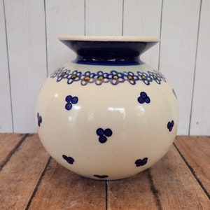 May include: A white ceramic vase with a blue and gold floral design. The vase has a round body and a flared rim.