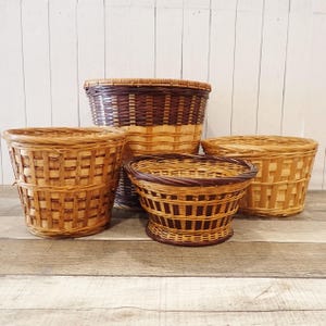 May include: Four woven baskets of varying sizes, made of natural brown and tan wicker. The baskets are arranged on a wooden surface.