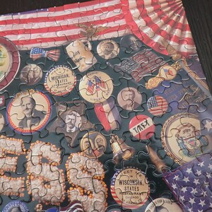 Może przedstawiać: Ukończone puzzle o tematyce patriotycznej. Elementy układanki przedstawiają obrazy amerykańskiej flagi, postaci historycznych i pamiątek w stylu vintage. Paleta kolor&oacute;w obejmuje kolory czerwony, biały, niebieski i złoty.