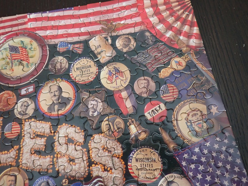 Może przedstawiać: Ukończone puzzle o tematyce patriotycznej. Elementy układanki przedstawiają obrazy amerykańskiej flagi, postaci historycznych i pamiątek w stylu vintage. Paleta kolor&oacute;w obejmuje kolory czerwony, biały, niebieski i złoty.