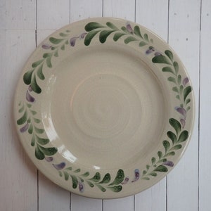 May include: A white ceramic plate with a green and purple floral design around the rim.