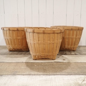 May include: Three natural woven wicker baskets with a light brown color. The baskets are sitting on a wooden surface.