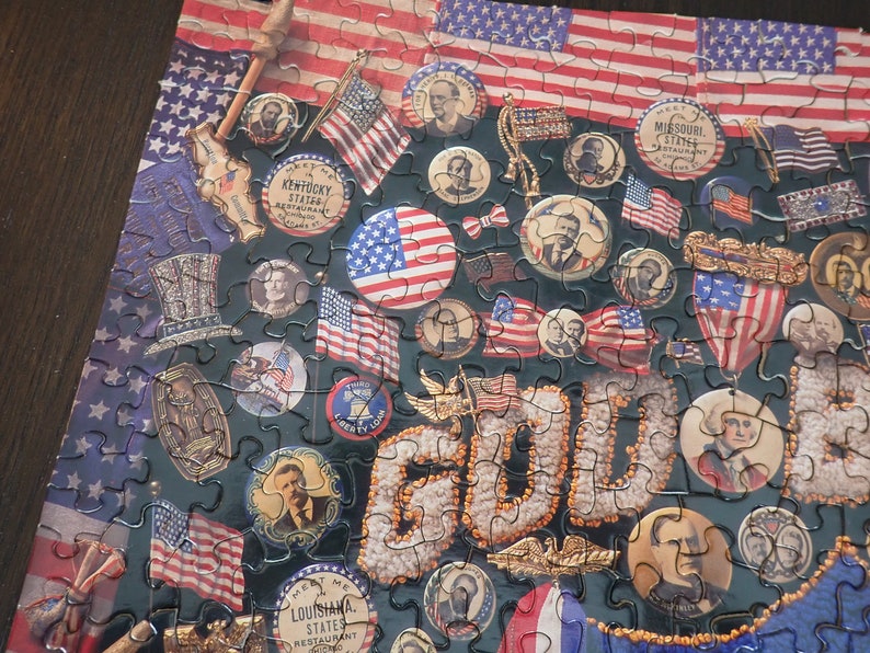 Może przedstawiać: Ukończone puzzle o tematyce amerykańskiej. Elementy układanki przedstawiają amerykańskie flagi, postacie historyczne i słowo "GOLD". Puzzle zawierają obrazy pieczęci stanowych i patriotyczne obrazy.