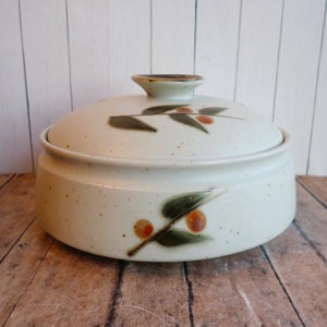 May include: A white ceramic casserole dish with a lid. The dish has a speckled glaze and a brown and green floral design.