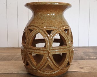 May include: A tan ceramic vase with a unique openwork design. The vase has a cylindrical body with geometric cutouts, a flared rim, and a speckled finish. The vase is approximately 7 inches tall.