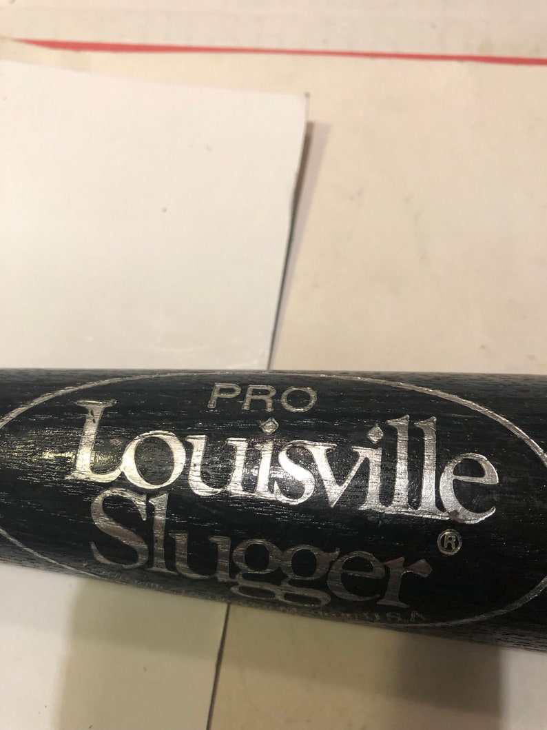 May include: Close-up of a black baseball bat with a silver "Louisville Slugger" logo and "PRO" written above it.