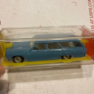 May include: A blue toy car in a clear plastic display case. The car has a white roof and is a station wagon style.