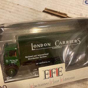 May include: A green toy truck with the words "London Carriers Limited" and "National and International Distribution Services" printed on the side. The truck is in a box with the words "EFE Exclusive First Editions" printed on it.