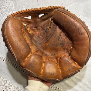 Könnte beinhalten: Ein abgenutzter, brauner Leder-Baseballhandschuh mit sichtbaren Nähten und den Texten "CUSTOM BUILT" und "MAJOR LEAGUERS". Der Handschuh hat die Prägungen "TRI", "FLEX" und "ACTION". Der Handschuh wird von einer Person gehalten.