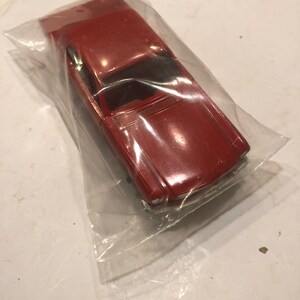 May include: A red toy car in a clear plastic bag. The car has a black windshield and a white front bumper.