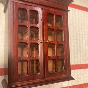 Op de afbeelding: Een donkerhouten kast met glazen deuren en een decoratieve rand. De kast heeft meerdere vierkante ruiten in elke deur.