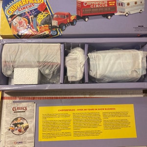 May include: A vintage toy set of a red and white circus wagon, a white trailer, and a red truck with a white cab. The set is packaged in a purple and white box with the words "Chipperfields Circus" on the front. The box also includes a pamphlet with the history of the Chipperfields Circus.