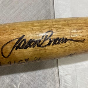 Puede incluir: Un bate de béisbol de madera con una firma negra que dice "Jason Brown".