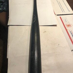 May include: A black wooden baseball bat with the text "GENUINE" and "PRO" printed on the side.