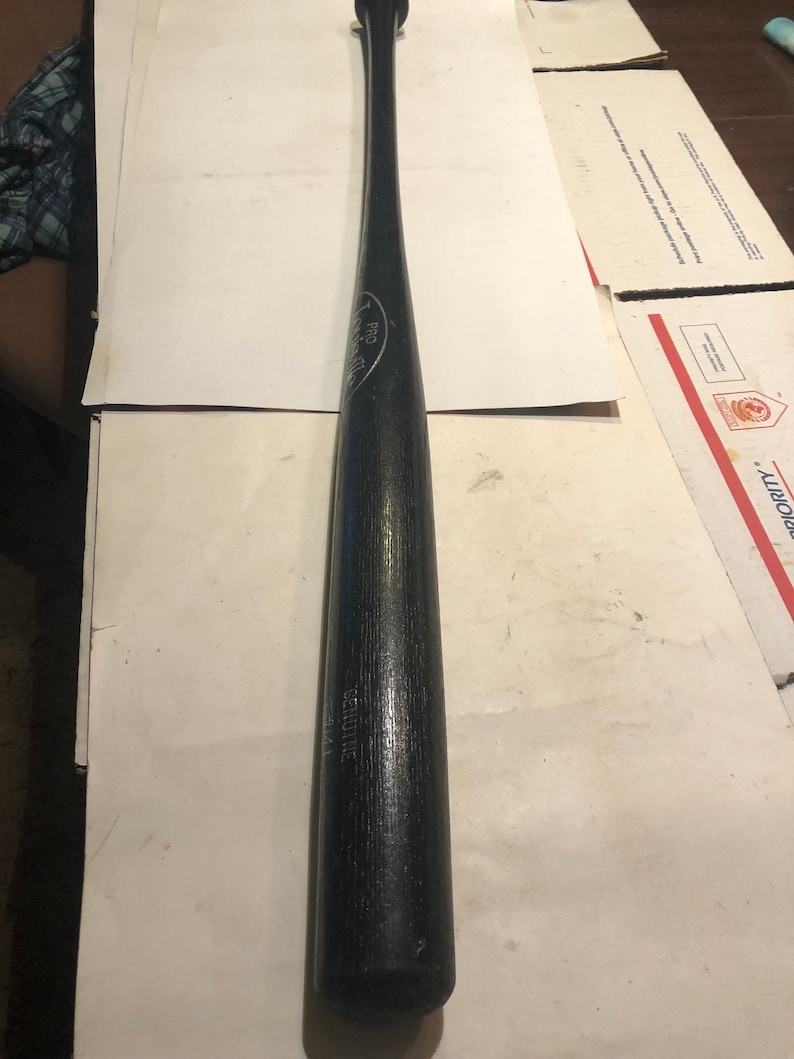 May include: A black wooden baseball bat with the text "GENUINE" and "PRO" printed on the side.