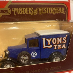 Puede incluir: Un modelo de juguete azul y blanco de una camioneta Ford modelo A de 1930 con las palabras "Lyons Tea" en el lateral. La camioneta tiene un techo blanco y un chasis negro. El modelo está en una caja roja y dorada con las palabras "Models of Yesteryear" en la parte delantera.