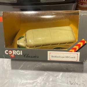 Puede incluir: Un autobús de juguete blanco y verde en una caja. La caja está etiquetada con "Corgi Classics" y "Bedford type OB Coach".