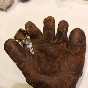 May include: A brown leather baseball glove with a worn and weathered appearance. The glove is open and the fingers are extended.