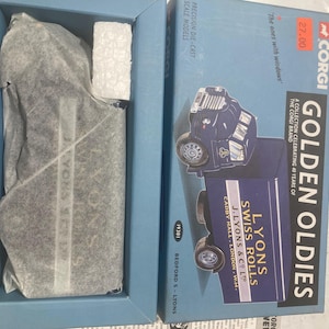 Puede incluir: Una caja azul y blanca para un camión modelo Corgi Golden Oldies. La caja presenta una imagen del camión, que es un camión Bedford S-type con una carrocería de entrega Lyons Swiss Rolls. La caja también incluye el texto "Corgi Golden Oldies", "The ones with windows", "A collection celebrating 40 years of the Corgi brand", "Lyons Swiss Rolls J. Lyons & Co. Ltd. Cadby Hall - London W.14", y "Bedford S - Lyons".