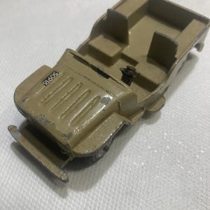 May include: A vintage toy jeep made of metal, painted in a light brown color. The jeep has a detailed interior with seats and a steering wheel. The number 50616 is printed on the hood.
